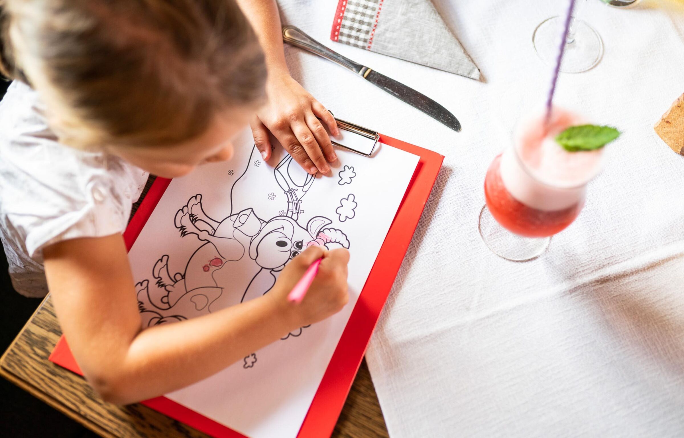 A child colors a coloring picture of a cow while waiting for food in a hut.