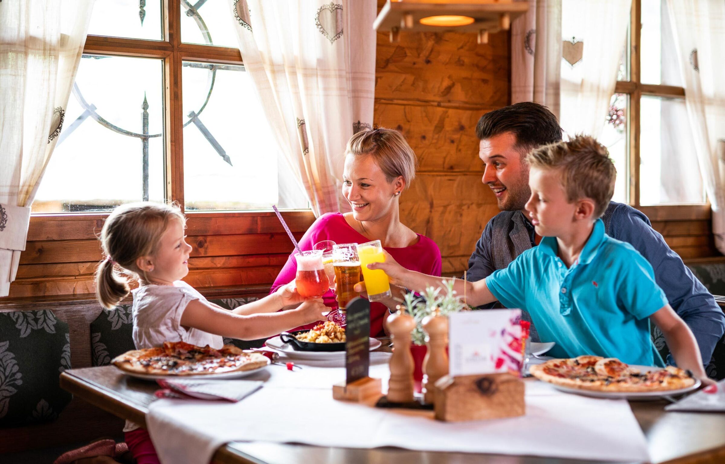 Eine Familie sitzt in einer Hütte und stoßen gerade mit Getränken