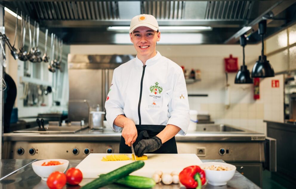 Un giovane cuoco è in piedi in cucina e taglia le verdure.
