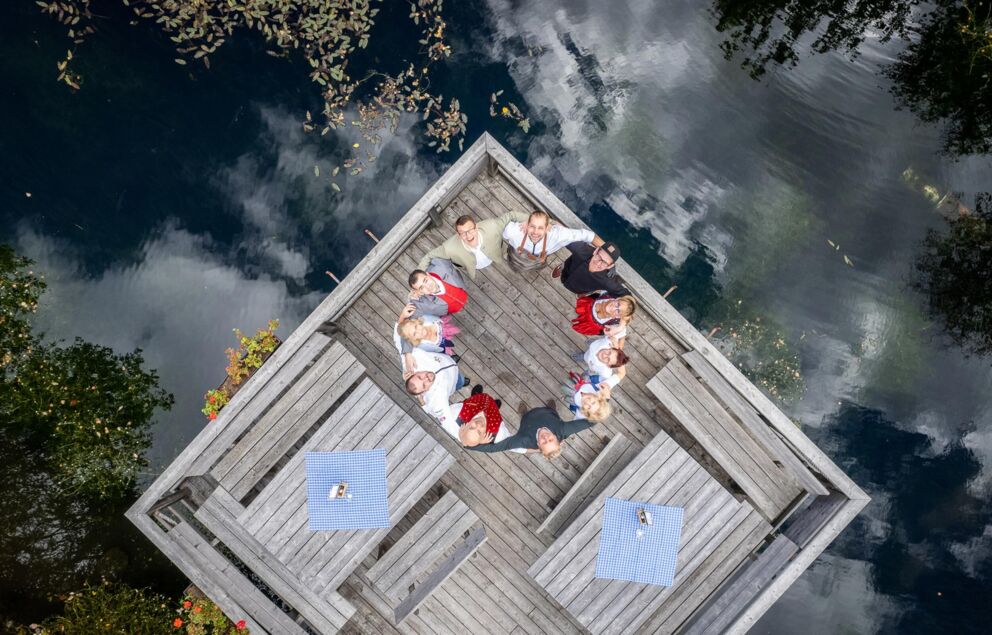Das Team vom Trattlerhof steht auf einem Floss am See und bilden umarmend einen Kreis.