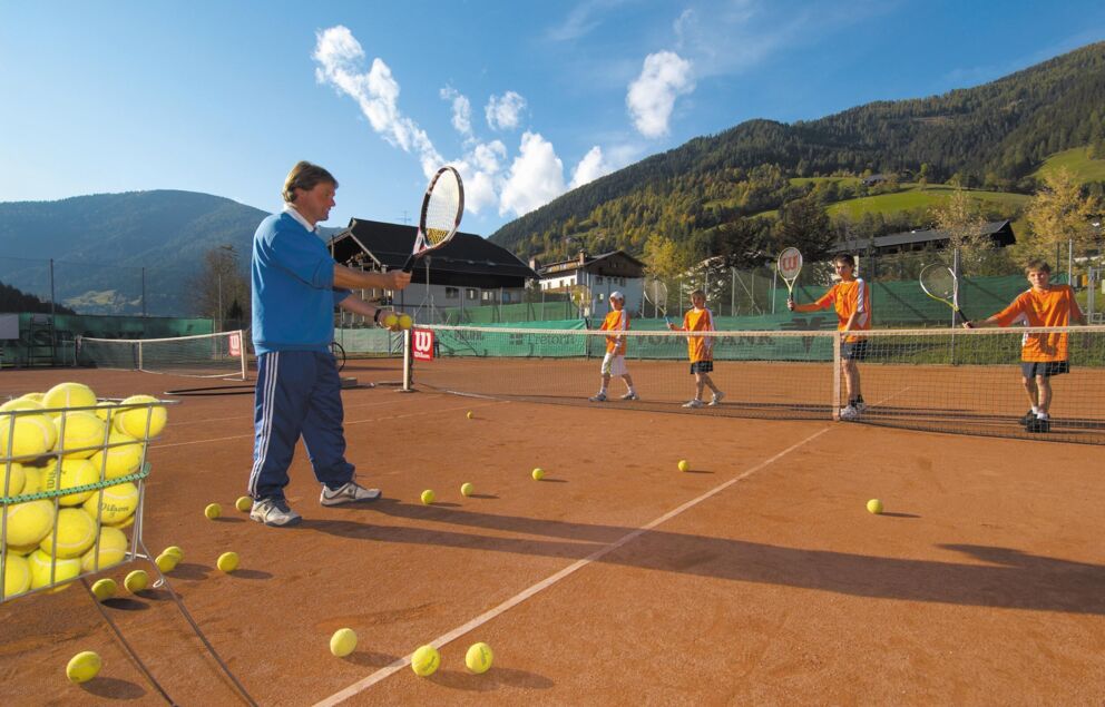Ein Tennislehrer lernt seinen Schülern Tennis, auf dem Boden liegen bereits ein paar Tennisbälle.