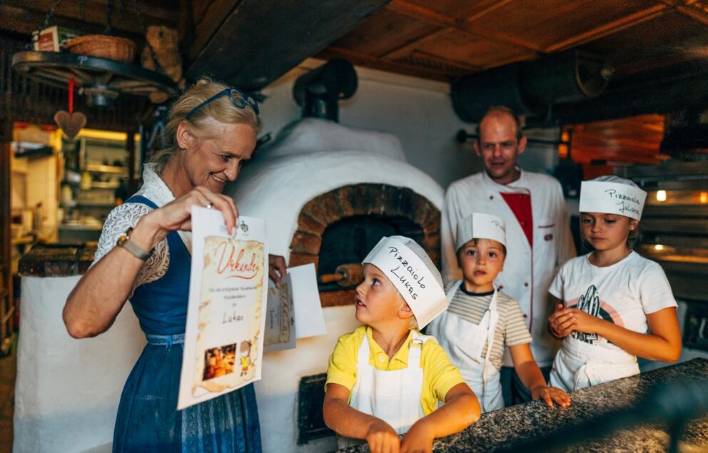 Drei Kinder mit Kochschürze und Mütze bekommen eine Urkunde für die Teilnahme am Pizza-Backkurs in Trattlers Einkehr in Bad Kleinkirchheim