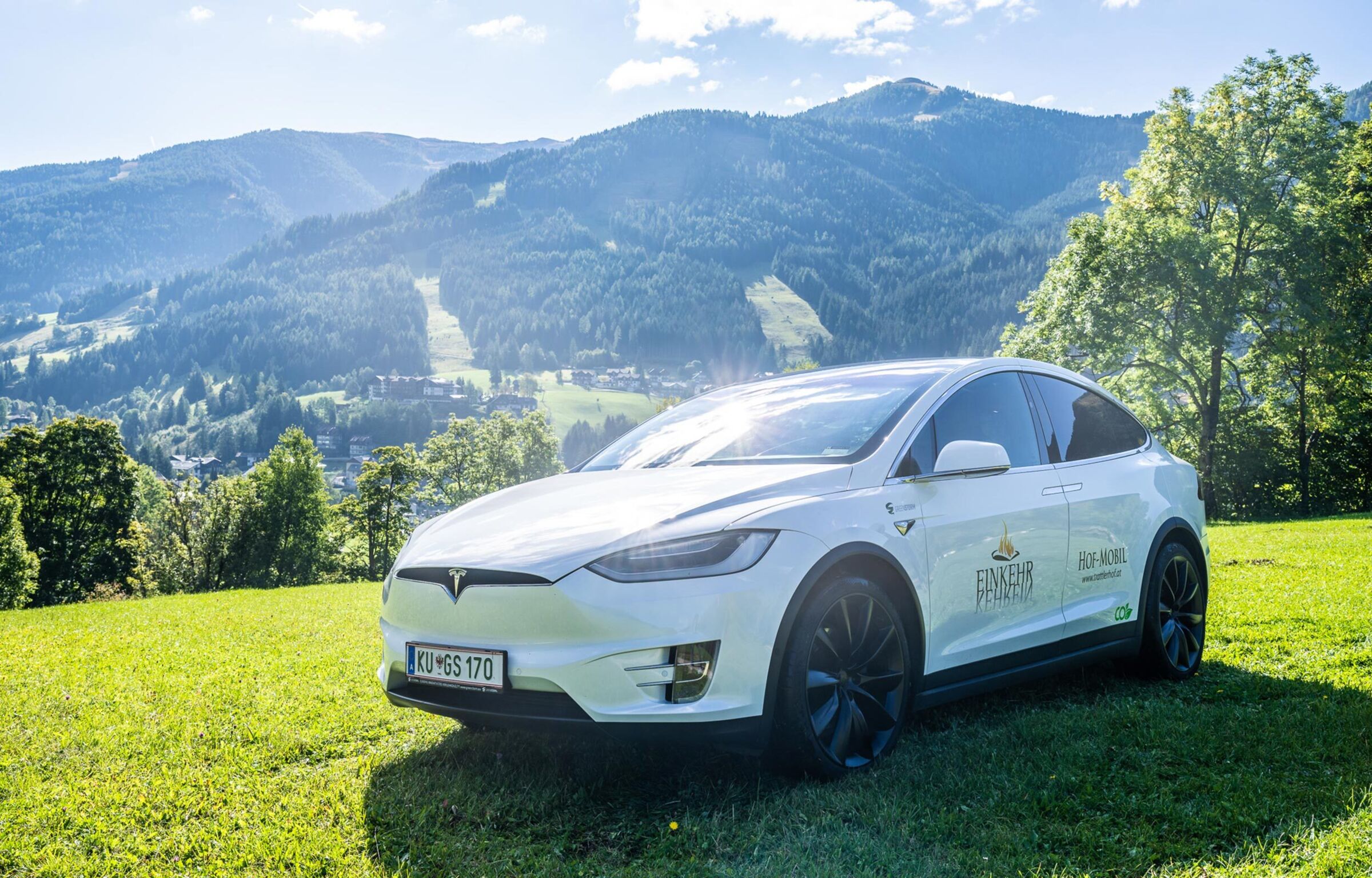 Ein weißer Tesla mit dem Trattlerhoflogo auf der Tür der Fahrerseite, steht auf einer Wiese.