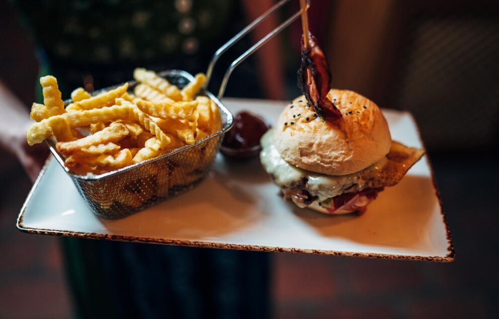 A burger with cheese and fries in a small fryer grid.