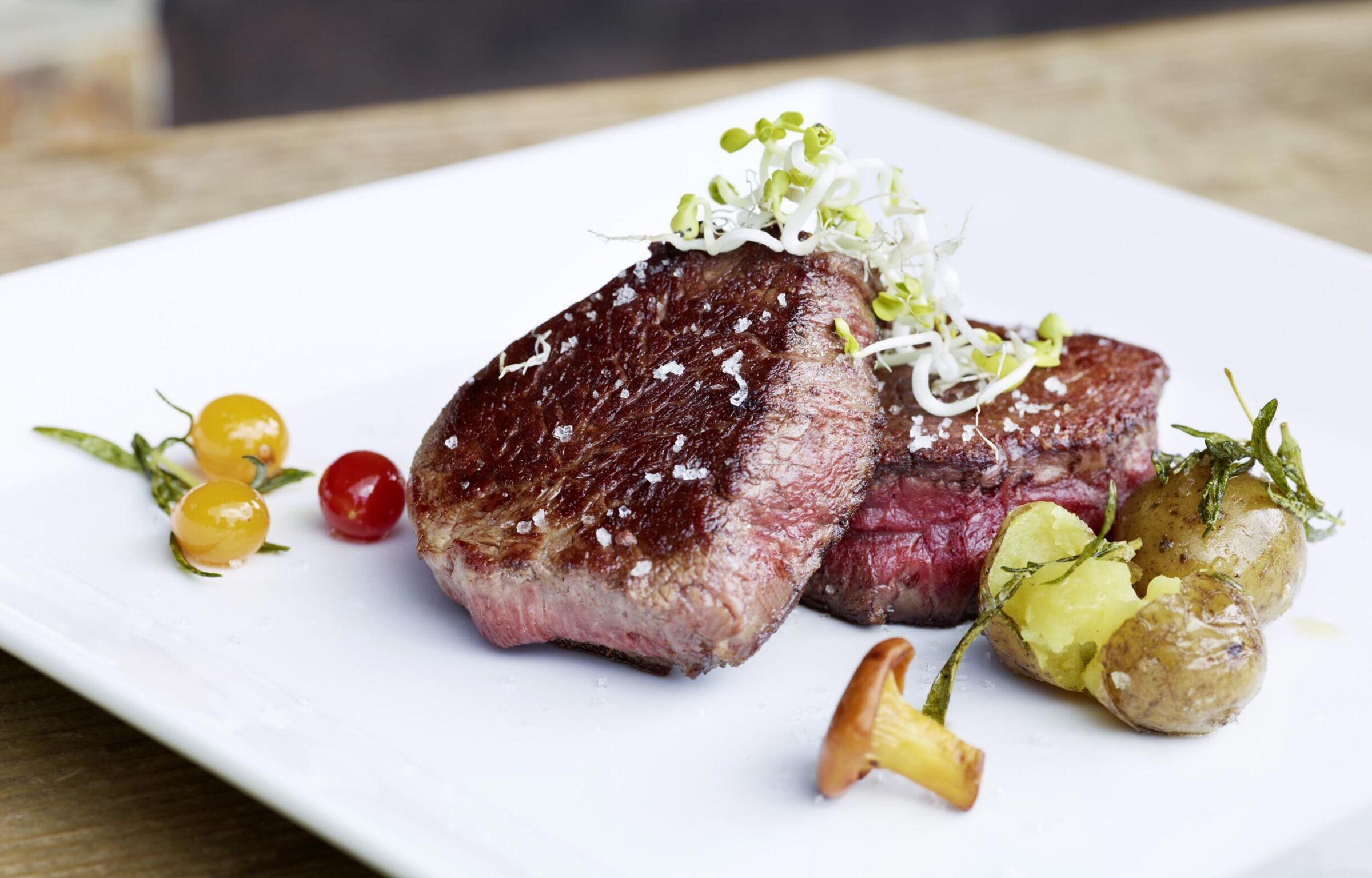 Steak on a plate with potatoes, a mushroom and watercress.