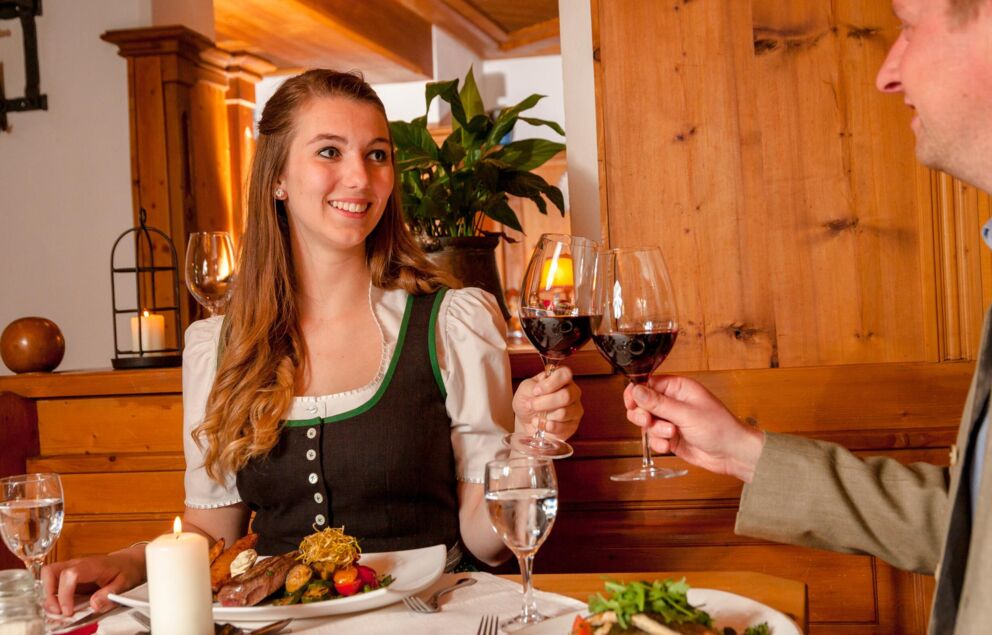 Ein Mann und eine Frau sitzen an einem Tisch und stoßen mit einem Glas Rotwein an.