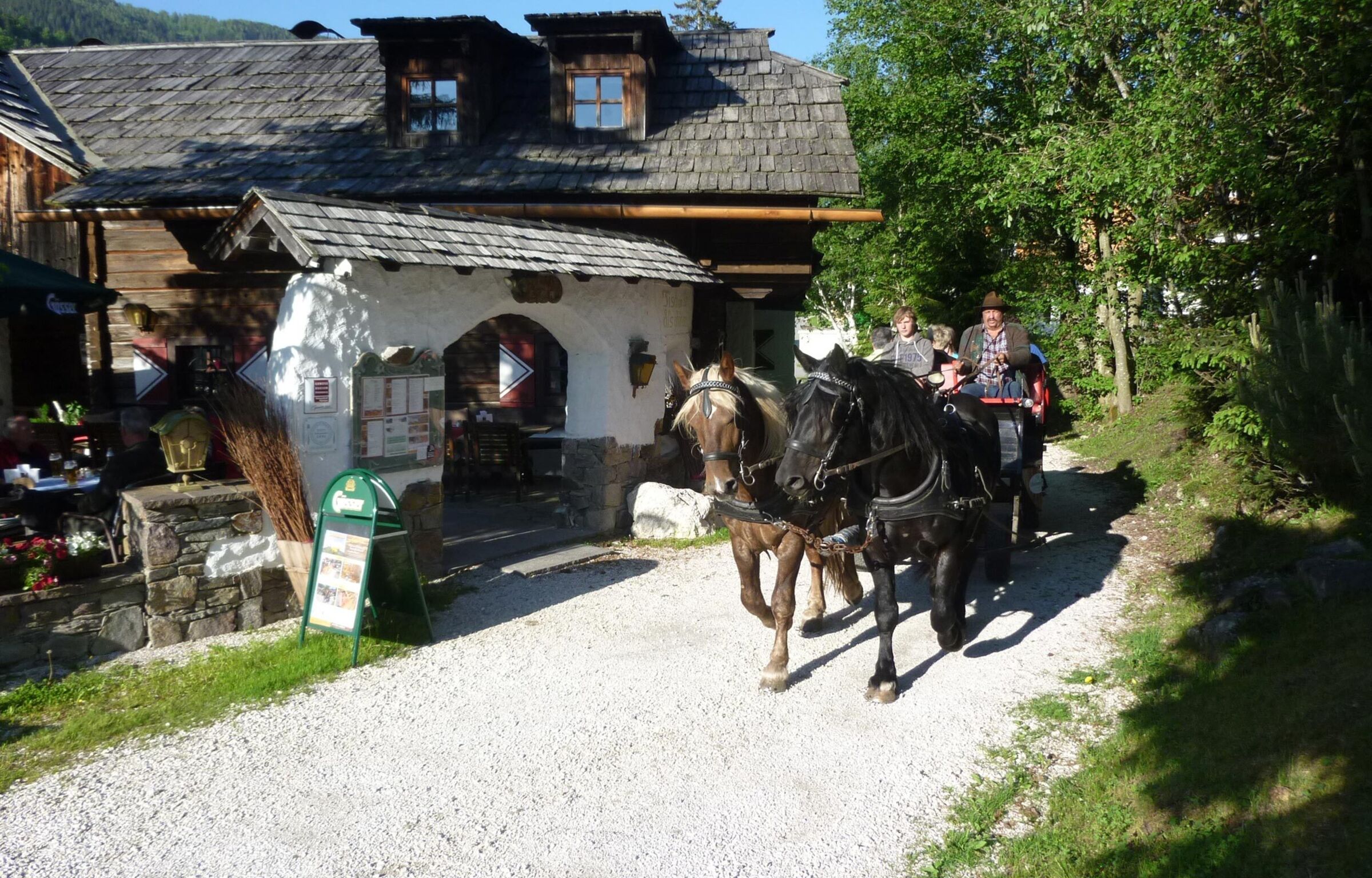 Eine Pferdekutsche fährt gerade an der Trattlers Einkehr vorbei.