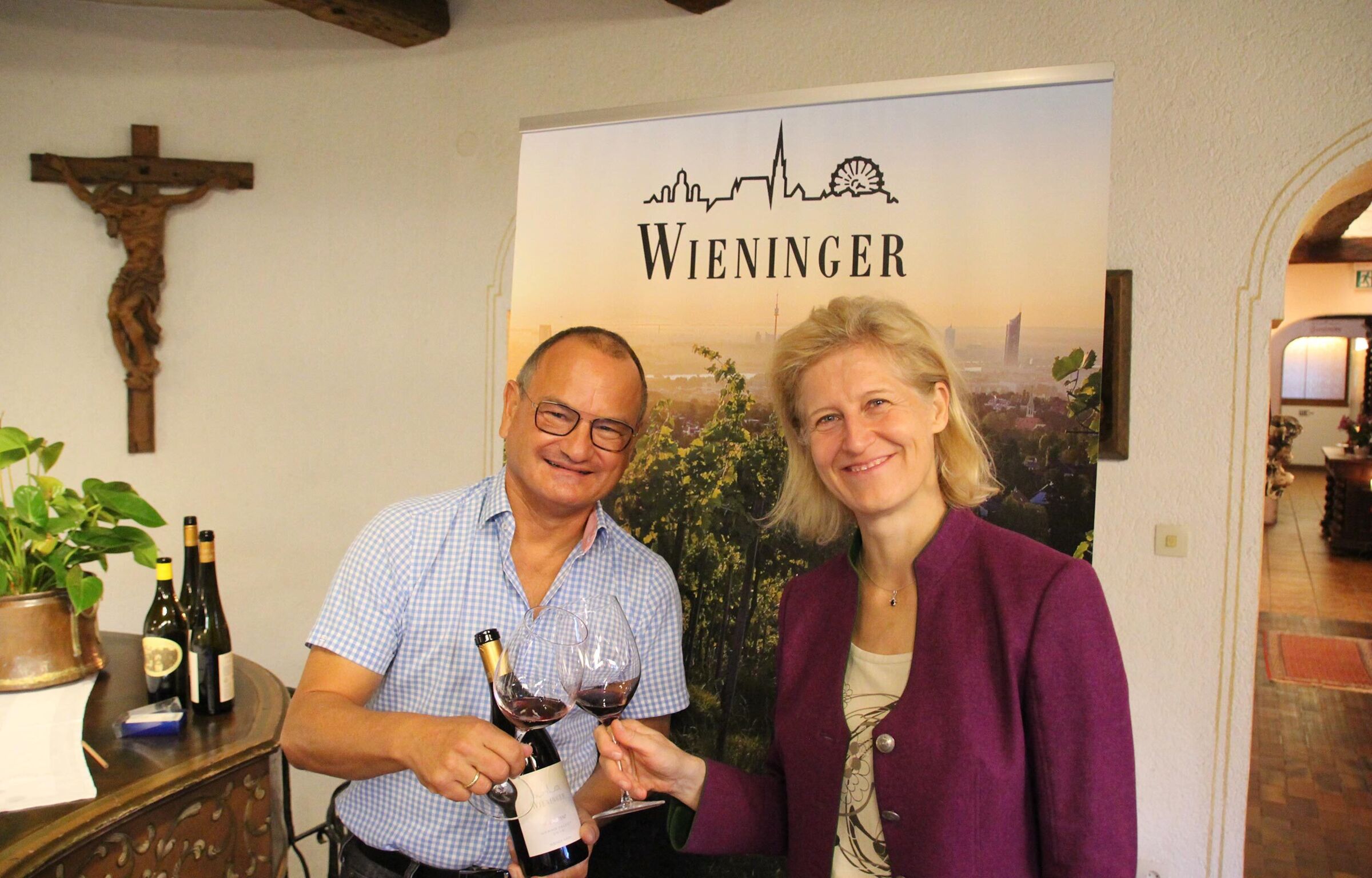 A man and a woman toast with a wine and laugh into the camera.