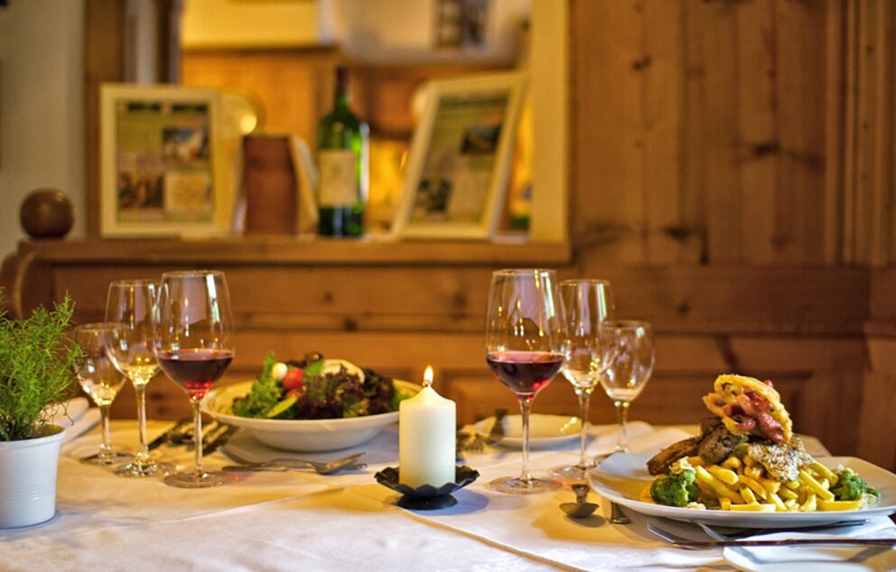 Ein gedeckter Tisch mit Wein, Burger mit Pommes und Salat in einem rustikalen Raum.