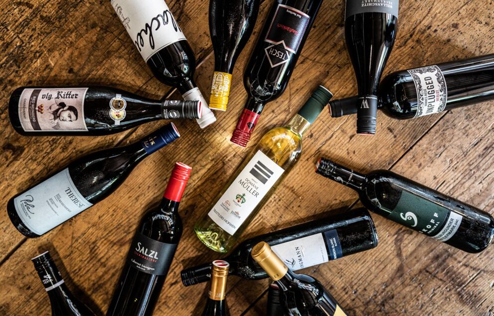 A large selection of wine bottles lie on a wooden floor