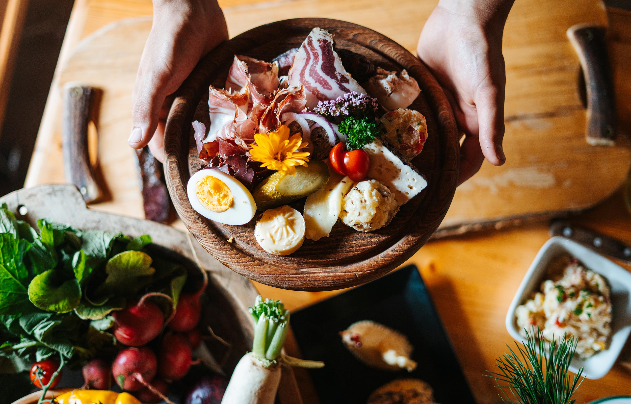 Someone holding a wooden board displaying bacon, eggs, cheese and other delicacies on it.